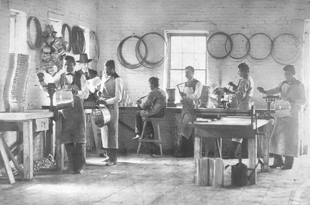 In this photo provided by the Carlisle Indian School Digital Resource Center, male students in the Carlisle Indian Industrial School pose for a photo in the tin shop with their instructor and Richard Henry Pratt. From left are Charles Oheltoint, Richard Henry Pratt, Henry Roman Nose, Paul Black Bear, instructor J.H. Curtain, Ernest, and Koba. (John N. Choate/Carlisle Indian School Digital Resource Center via AP)