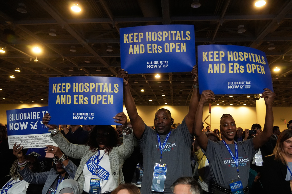 FILE - People supporting Billionaire Tax Now hold up signs at the 2026 California Democratic Party State Convention in San Francisco, Feb. 21, 2026. (AP Photo/Jeff Chiu, File)