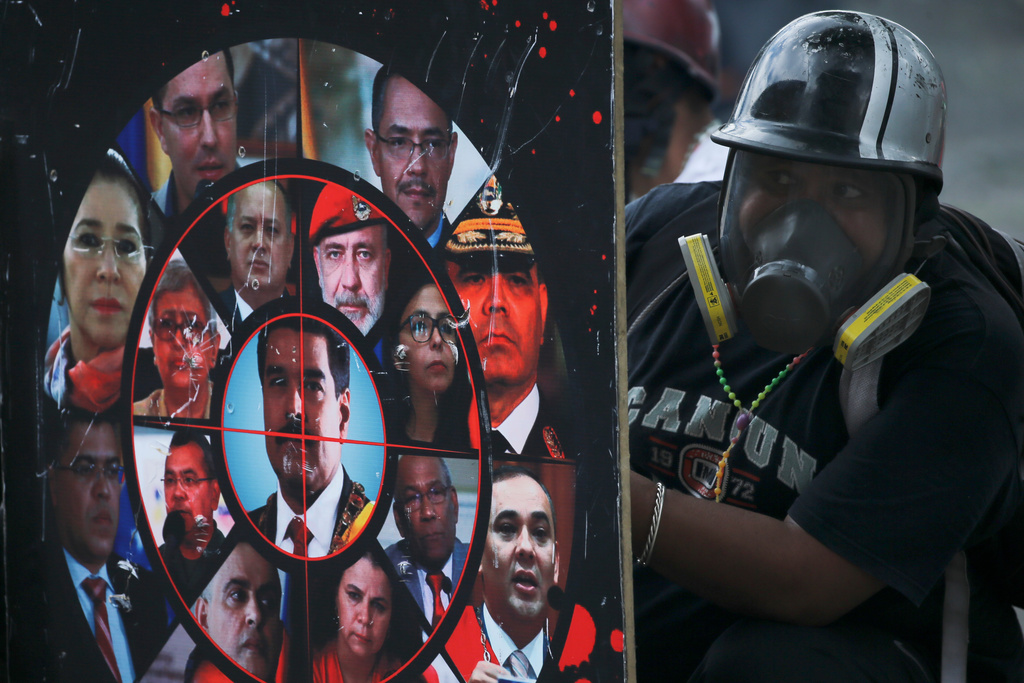 FILE - An anti-government protester opposing President Nicolas Maduro's plan to rewrite the constitution, holds a homemade shield brandished with photos of Maduro, government officials and a gun sight, during clashes with security forces blocking a march to the Supreme Court, in Caracas, Venezuela, July 22, 2017. (AP Photo/Fernando Llano, File)