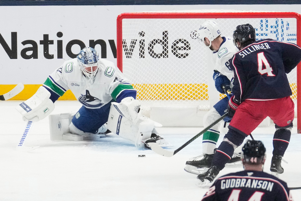 Vancouver Canucks goaltender Kevin Lankinen (32) blocks a shot by Columbus Blue Jackets center Cole Sillinger (4) next to center Max Sasson (63) in the first period of an NHL hockey game Thursday, Jan. 15, 2026, in Columbus, Ohio. (AP Photo/Sue Ogrocki)