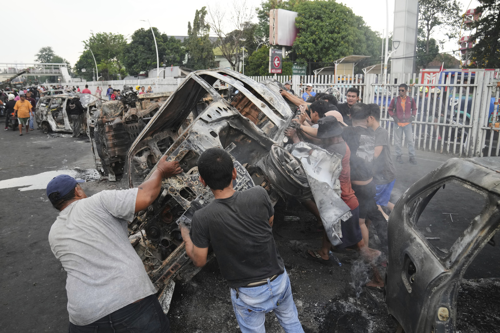 People overturn the wreckage of a car burned in violent protests against lawmakers' allowance and alleged police brutality after a delivery rider was run over by a police armored vehicle during clashes between riot police and students protesters, in Jakarta, Indonesia, Saturday, Aug. 30, 2025. (AP Photo/Dita Alangkara)