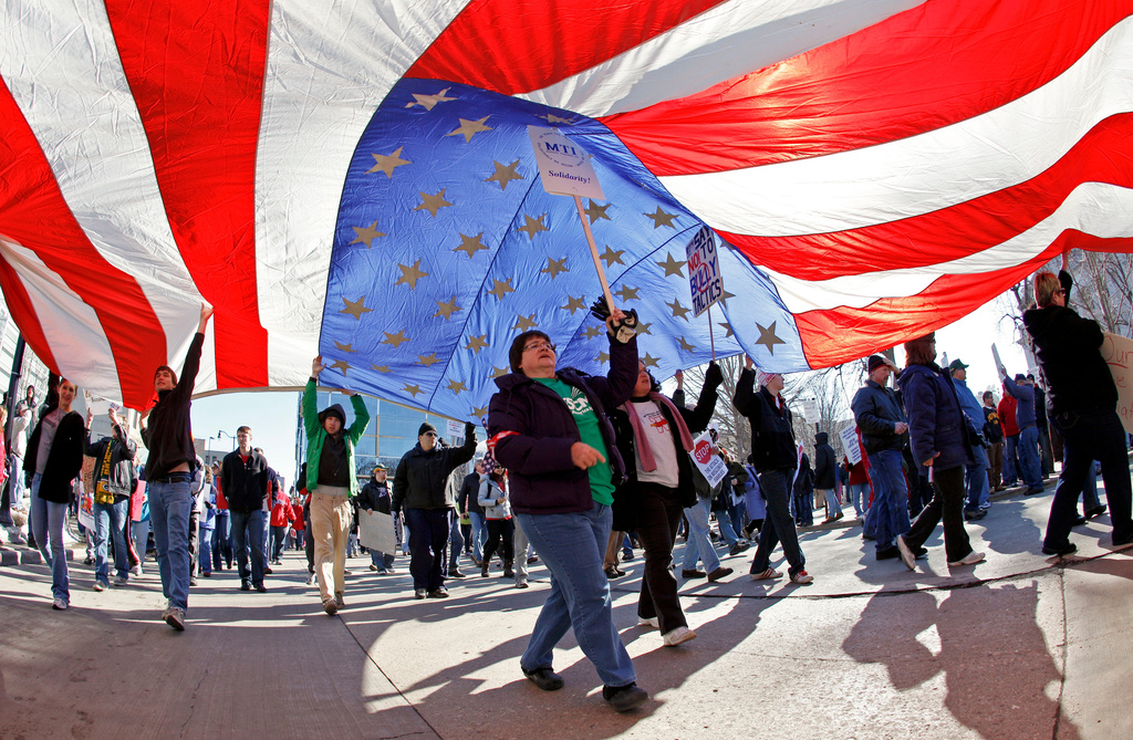 FILE - AFSCME member Merryann Wen helps hold up an American flag as she marches around the Capitol Square in Madison, Wis., Feb. 19, 2011. (AP Photo/Andy Manis, File)