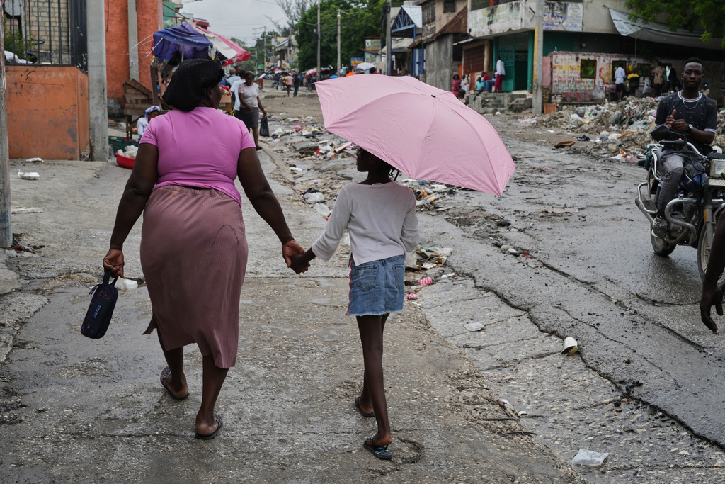 A woman holds a girl with an umbrella's hand during light rain in Port-au-Prince, Haiti, Thursday, Oct. 23, 2025. (AP Photo/Odelyn Joseph)