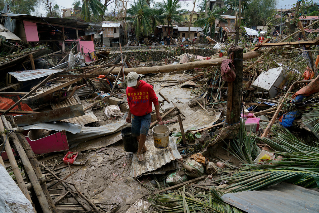 FILE -A man carries pails beside damaged homes due to Typhoon Rai in Talisay, Cebu province, central Philippines on, Dec. 17, 2021. (AP Photo/Jay Labra, File)