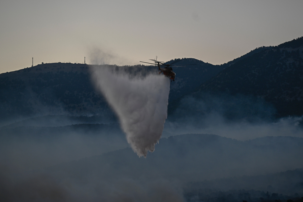 A firefighting helicopter drops water over a smoke-filled forest during a wildfire near Porto Germeno, northwest of Athens, Greece, Sunday, Aug. 2, 2026. (AP Photo/Michael Varaklas)