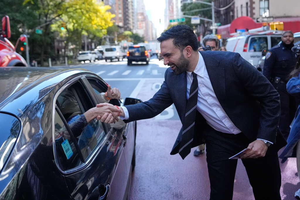New York City mayoral candidate Zohran Mamdani greets some people in a car while surrounded by reporters in New York, Monday, Oct. 27, 2025. (AP Photo/Seth Wenig)