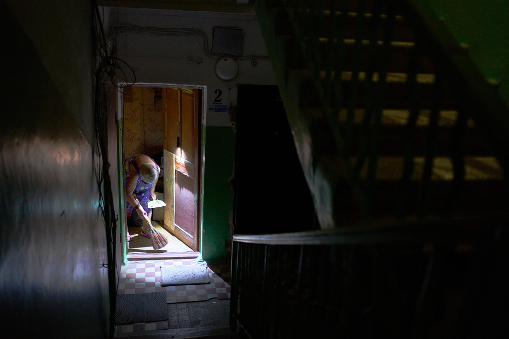 Larysa Polishchuk, 76, cleans the entrance of her apartment in a partially damaged residential building the day after a Russian missile and drone attack in Kyiv, Friday, Aug. 21, 2026. (AP Photo/Francisco Seco)