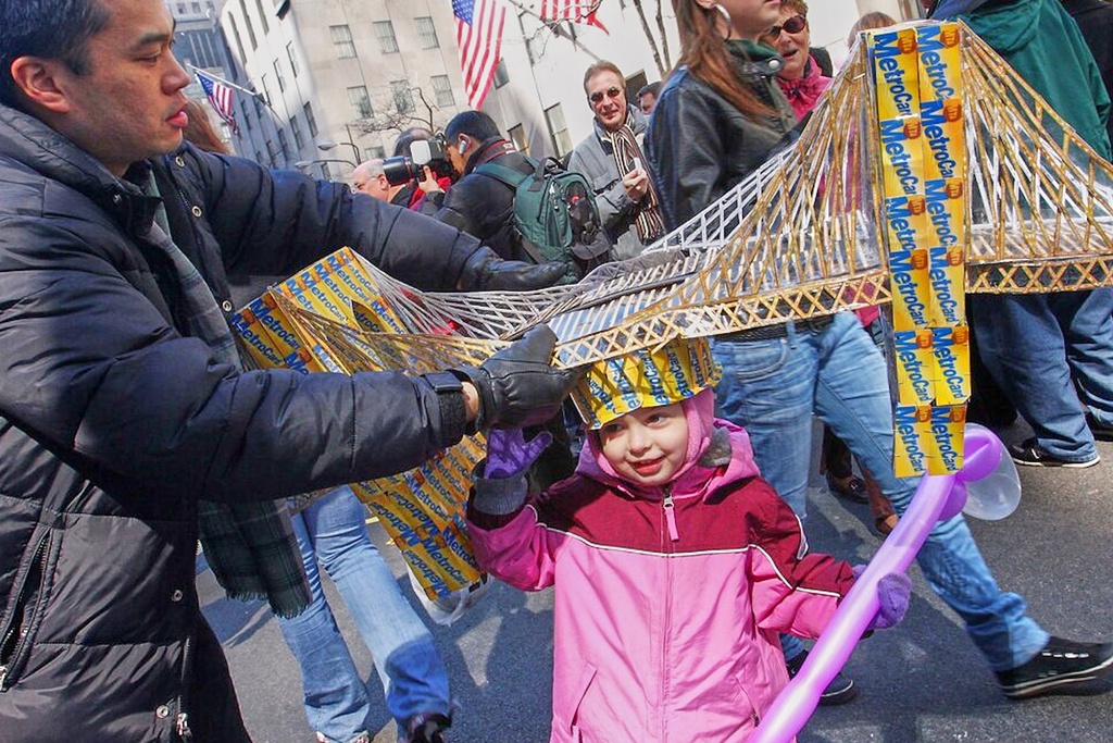 FILE - Russell Chin, left, helps Angie Hoyle, 3, of the Brooklyn borough of New York, as she tries on a hat made of MetroCards shaped as the Brooklyn Bridge during the Easter Parade on New York's Fifth Avenue, March 23, 2008. (AP Photo/Tina Fineberg, File)