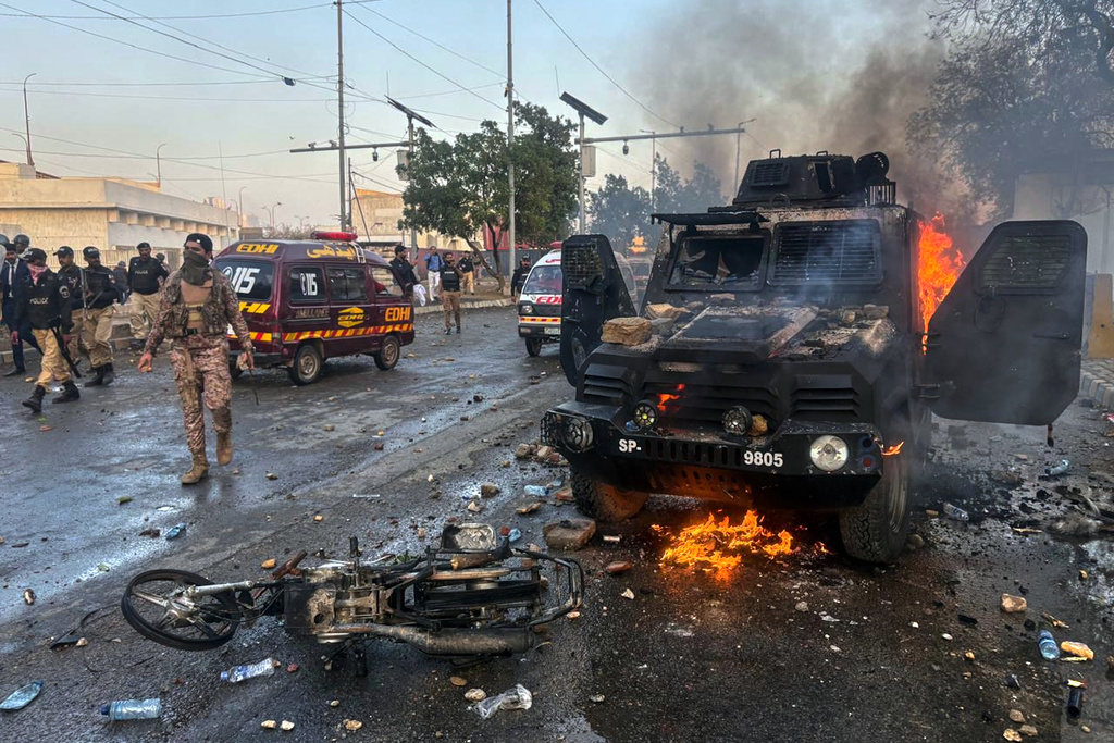 Paramilitary soldiers and police officers walk past a burning police's armoured vehicle, which was set on fire by Shiite Muslims during a protest over the killing of Iranian Supreme Leader Ayatollah Ali Khamenei, in Karachi, Pakistan, Sunday, March 1, 2026. (AP Photo/Muhammad Farooq)