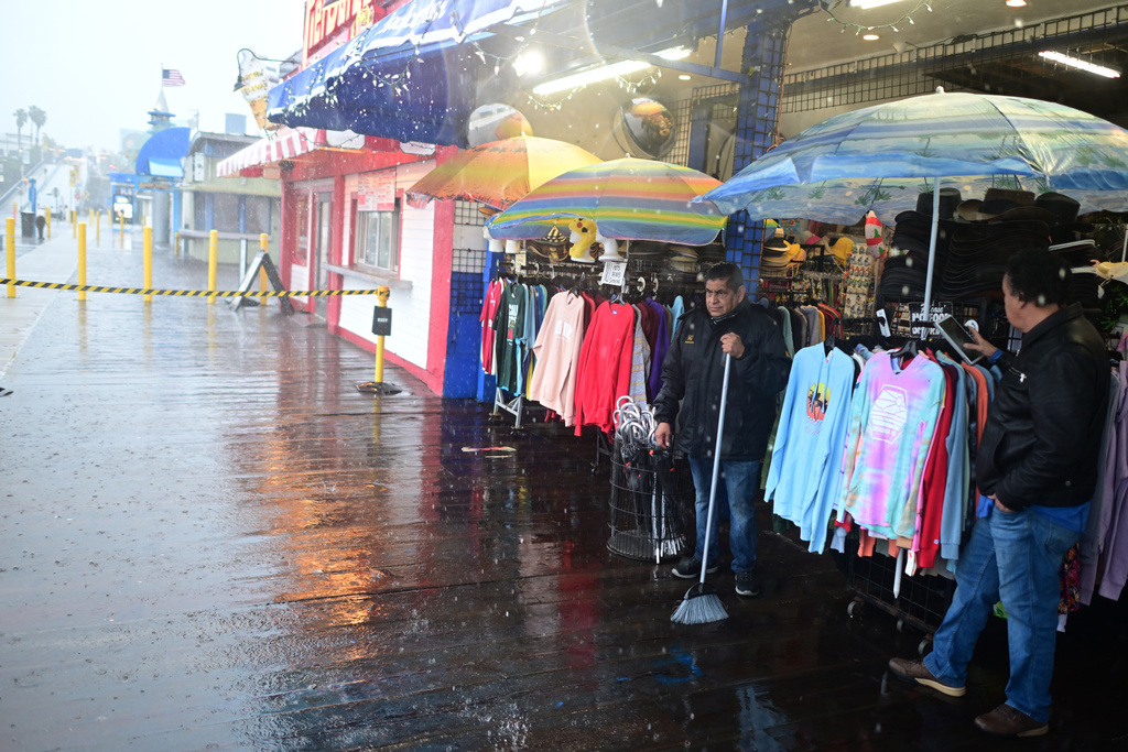 Miguel Lopez sweeps water from Marlene's Beachcomber on the Santa Monica pier Wednesday, Dec. 24, 2025, in Santa Monica, Calif. (AP Photo/Wally Skalij)