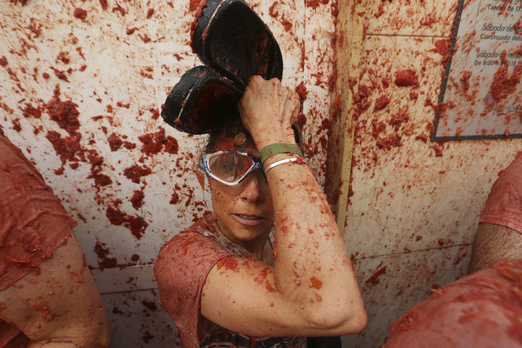 A woman covers herself as revelers throw tomatoes at each other during the annual "Tomatina" tomato fight fiesta, in the village of Bunol near Valencia, Spain, Wednesday, Aug. 27, 2025. (AP Photo/Alberto Saiz)