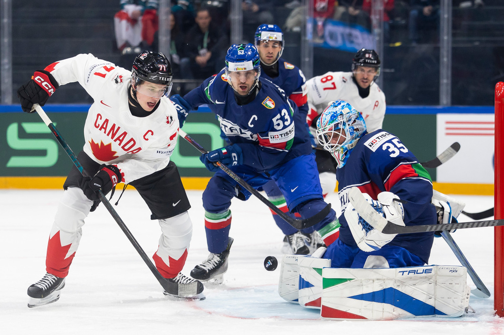 Canada's Macklin Celebrini, left, vies for the puck against Italy's Alex Trivellato, center, and Italy's goaltender Davide Fadani, right, during the 2026 IIHF Men's Ice Hockey World Championship preliminary round group B game between Italy and Canada, in Fribourg, Switzerland, Saturday, May 16, 2026. (Cyril Zingaro/Keystone via AP)