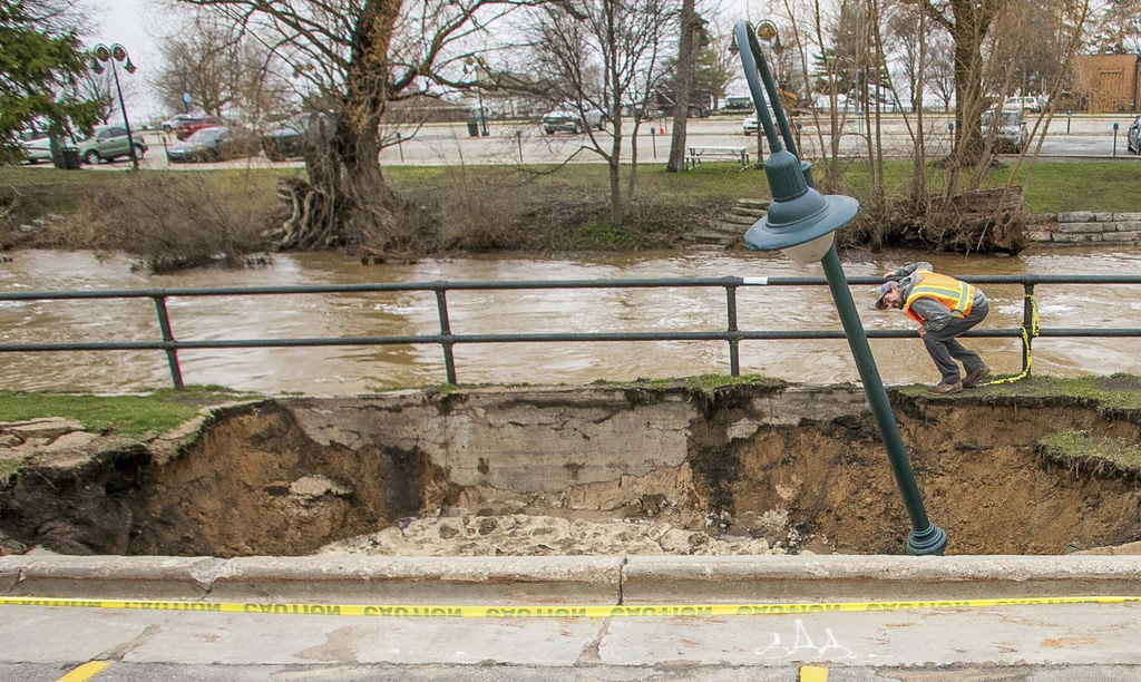 City Streets Department workers inspect a sinkhole that swallowed a street light and parts of a sidewalk along the surging Boardman/Ottaway River on Wednesday, April 15, 2026, in downtown Traverse City, Mich. (Jan-Michael Stump/Traverse City Record-Eagle via AP)
