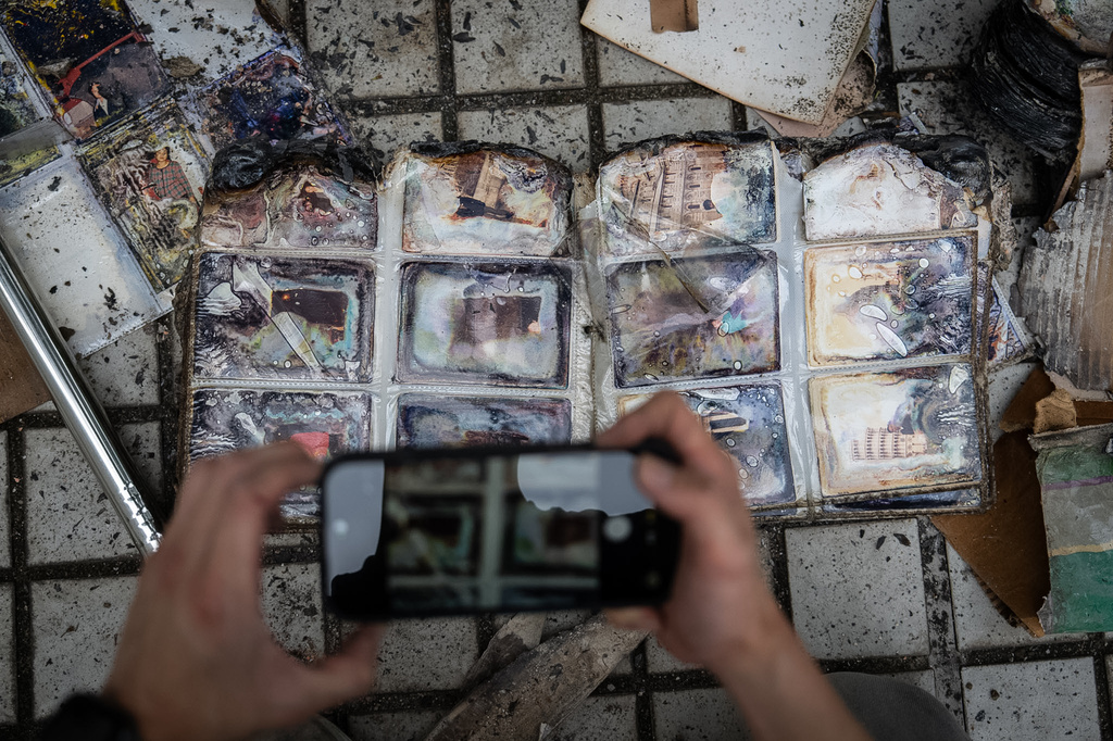 A member of the Mak family takes pictures of a charred family album found at their flat at Wang Fuk Court during an interview, in Hong Kong, Monday, April 20, 2026. (AP Photo/ Chan Long Hei)