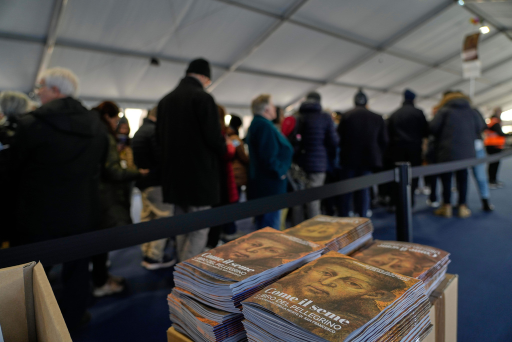 Pilgrims pass through security checks as they queue to honor the bones of St. Francis during the first public display inside the St. Francis Basilica, marking the 800th anniversary of the saint's death, in Assisi, Italy, Sunday, Feb. 22, 2026. The booklet with an image is St. Francis reads: "Like the seed, booklet of the pilgrim". (AP Photo/Gregorio Borgia)