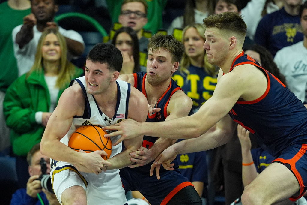 Virginia's Thijs de Ridder, left and Dallin Hall, center, force a jump ball with Notre Dame forward Brady Koehler (6) during overtime in an NCAA college basketball game in South Bend, Ind., Tuesday, Jan. 27, 2026. (AP Photo/Michael Conroy)