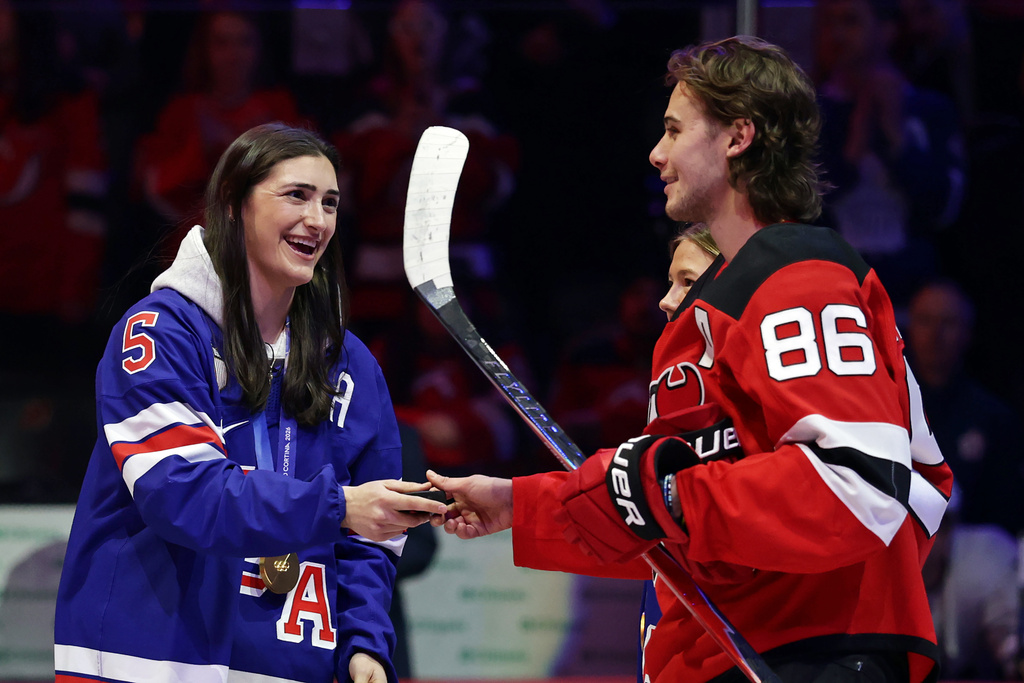 New Jersey Devils center Jack Hughes (86) gives United States women's gold medal hockey players Megan Keller the puck after a ceremonial puck drop before an NHL hockey game Wednesday, March 4, 2026, in Newark, N.J. (AP Photo/Adam Hunger)
