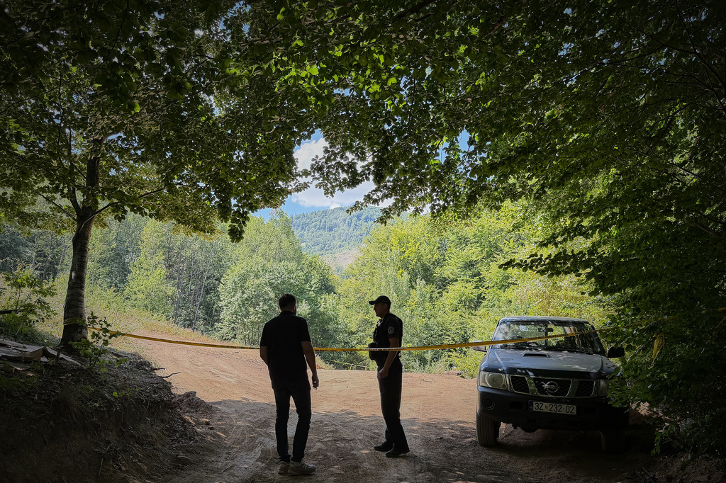 Erblin Ademi, left, whose father, Adem Ademi, a prominent surgeon, disappeared along with 22 other intellectuals during the Kosovo war in April 1999, speaks to a police officer near the excavation site of a mass grave in Small Kalluder, Kosovo, Wednesday, Aug. 5, 2026. (AP Photo/Zana Cimili)