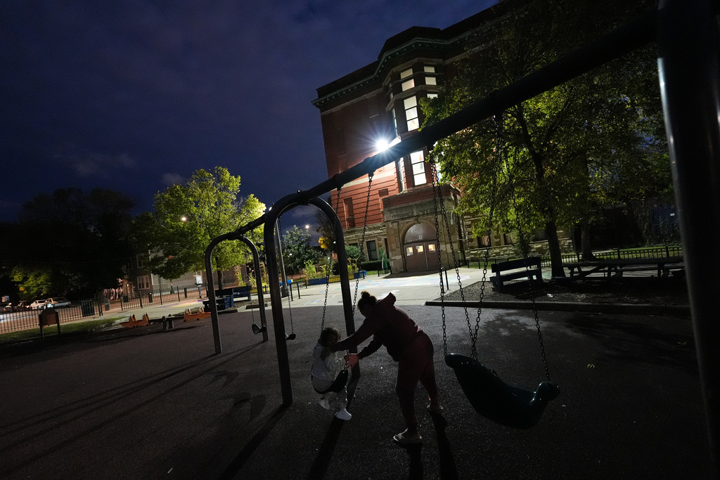 A mother pushes her daughter on a swing at Funston Elementary School as night falls, in Chicago's Logan Square neighborhood, Tuesday, Oct. 14, 2025. (AP Photo/Rebecca Blackwell)