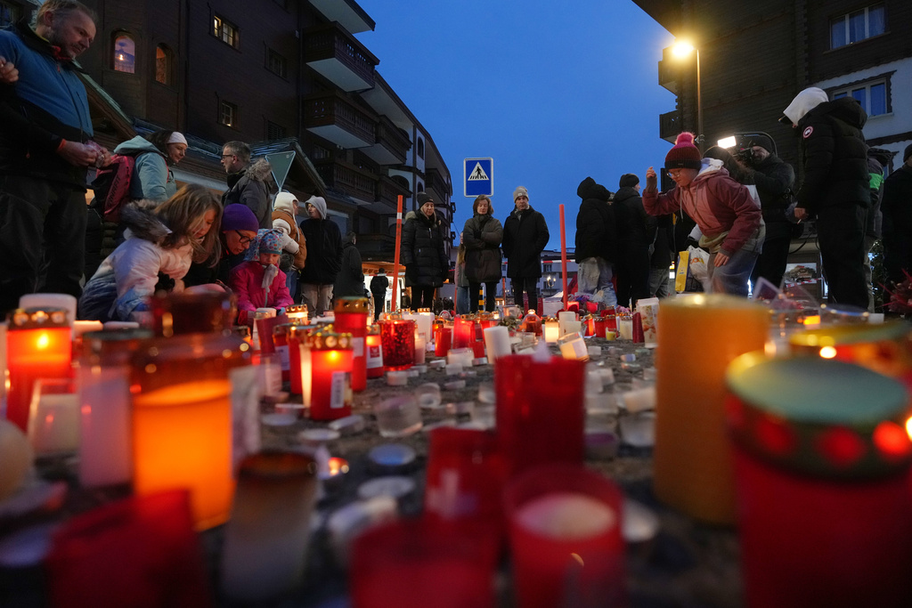 People light candles near the sealed off Le Constellation bar in Crans-Montana, Swiss Alps, Switzerland, Friday, Jan. 2, 2026, where a devastating fire left dead and injured during the New Year's celebrations. (AP Photo/ Antonio Calanni)