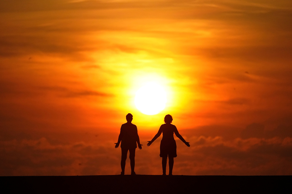 FILE - A couple stands on a jetty as the sun rises over the Atlantic Ocean in Bal Harbour, Fla., Sept. 19, 2020. (AP Photo/Wilfredo Lee, File)