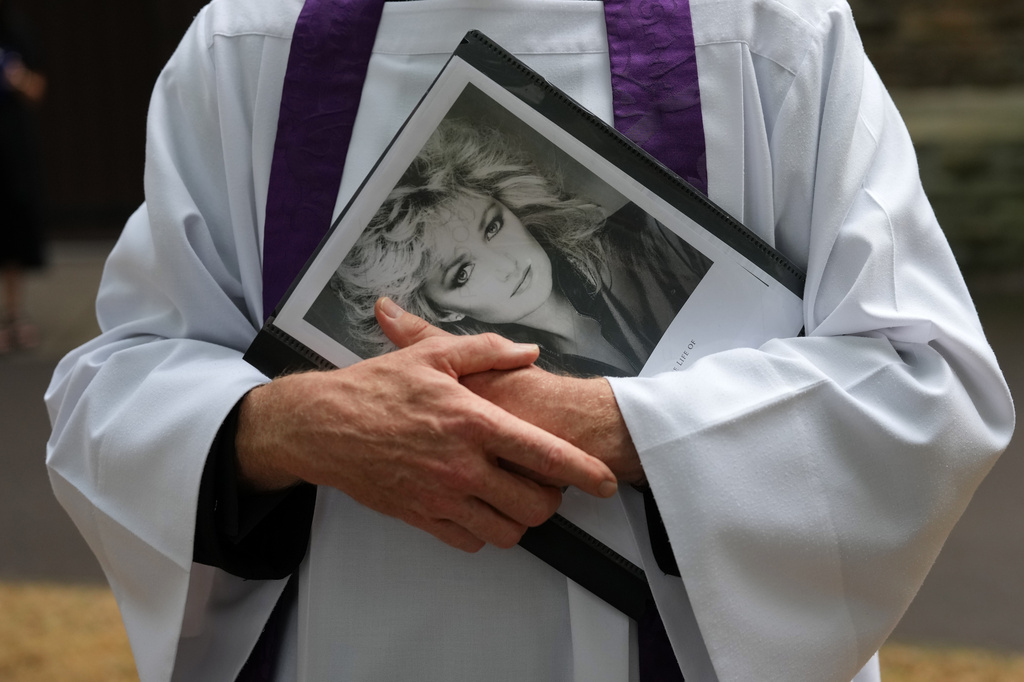 An unidentified priest holds a Bonnie Tyler poster outside St. Mary's Church in Swansea, Wales, Monday, Aug. 17, 2026 before the service and funeral of the musician, whose real name was Gaynor Hopkins. (AP Photo/Alastair Grant)