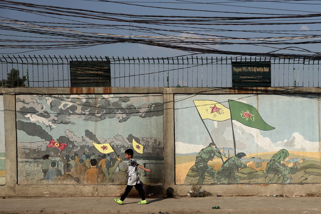 A boy walks past murals depicting Kurdish YPG and YPJ fighters battling Islamic State militants in Qamishli, northeastern Syria, Wednesday, Aug. 26, 2026. (AP Photo/Baderkhan Ahmad)