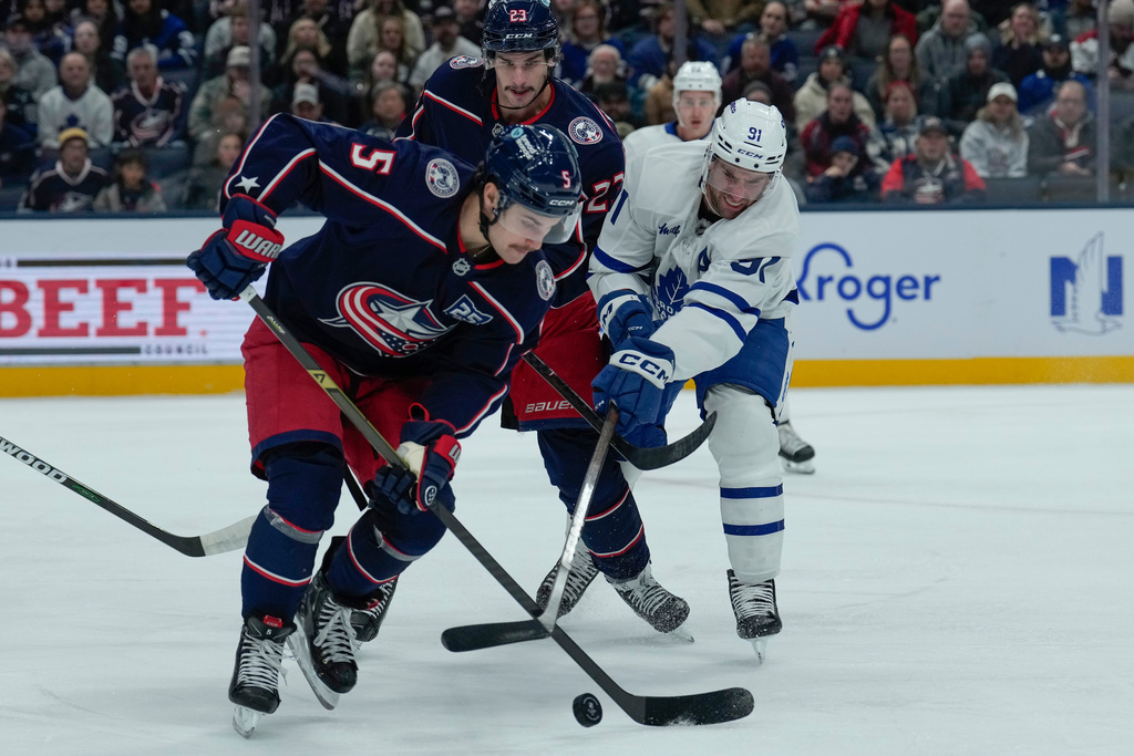 Columbus Blue Jackets defenseman Denton Mateychuk (5) and center Sean Monahan (23) battle for the puck with Toronto Maple Leafs center John Tavares (91) in the first period of an NHL hockey game, Wednesday, Nov. 26, 2025, in Columbus. (AP Photo/Carolyn Kaster)
