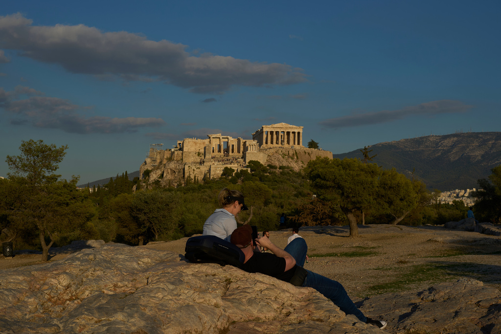 Tourist rest at Pnyx as the 5th century B.C. Parthenon temple stands free of scaffolding on the Acropolis hill in Athens, Friday, Oct. 10, 2025, after the removal of restoration structures that had covered parts of the ancient monument for decades.(AP Photo/Petros Giannakouris)