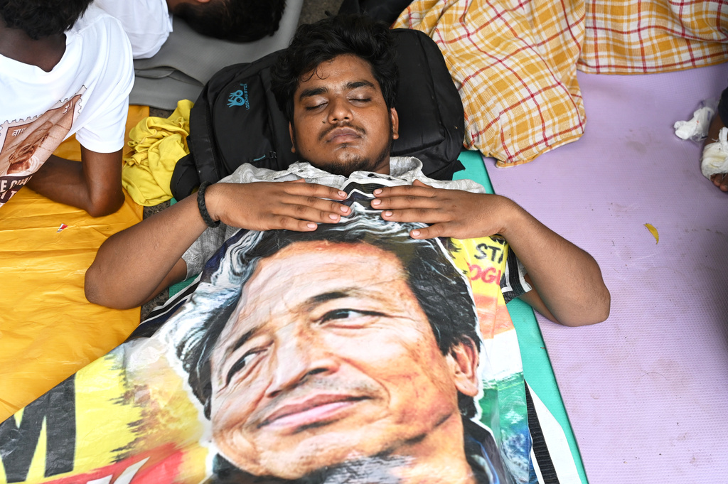 A reclining protestor covers himself with a banner printed with a portrait of Sonam Wangchuk, a prominent activist who was forcefully transferred to a hospital by the police as he staged a hunger strike in support of a movement led by Cockroach Janta Party, at a protest in New Delhi, India, Wednesday, July 22, 2026. (AP Photo/Vipin)