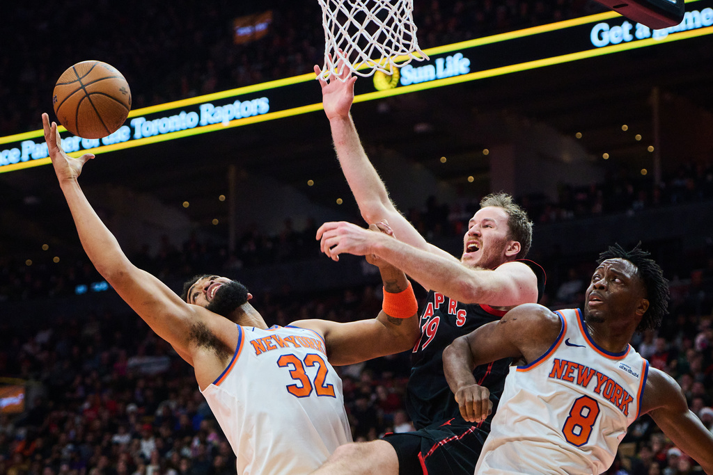 Toronto Raptors' Jakob Poeltl (19) is stopped at the net by New York Knicks' Karl-Anthony Towns (32) and New York Knicks' OG Anunoby (8) during the first half of an NBA Cup basketball game in Toronto, Tuesday, Dec. 9, 2025. (Sammy Kogan/The Canadian Press via AP)