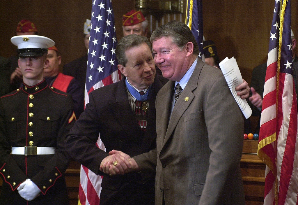 FILE - Retired Maj. Gen. Patrick Brady, center left, shakes hands with Rep. Randy "Duke" Cunningham, R-Calif., after Cunningham spoke in support of the "Flag Protection Constitutional Amendment," on Capitol Hill, March 13, 2001, in Washington. (AP Photo/Dennis Cook, File)