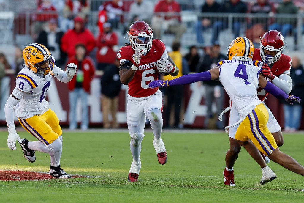 Oklahoma running back Tory Blaylock (6) runs the ball between LSU safety Tamarcus Cooley (0) and cornerback Mansoor Delane (4) for a first down during the first half of an NCAA college football game Saturday, Nov. 29, 2025, in Norman, Okla. (AP Photo/Alonzo Adams)