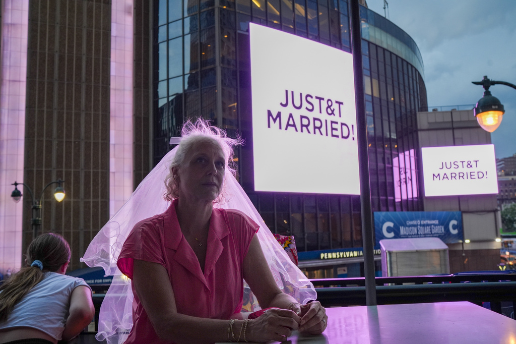 A Taylor Swift fan wearing a wedding veil sits at a restaurant next to Madison Square Garden where a "JUST&T MARRIED" sign is displayed during a wedding between singer Taylor Swift and National Football League player Travis Kelce on Friday, July 3, 2026, in New York. (AP Photo/Ryan Murphy)