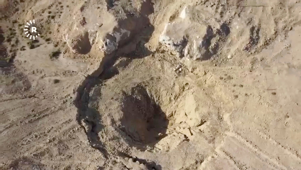 In this image taken from video provided by Rudaw TV, an aerial view shows a sinkhole at the Khasfa site near the northern Iraqi city of Mosul, where authorities have begun excavating a mass grave believed to contain thousands of victims of the Islamic State (IS) Mosul, Iraq, Sunday, Aug. 17, 2025. (Rudaw TV via AP)