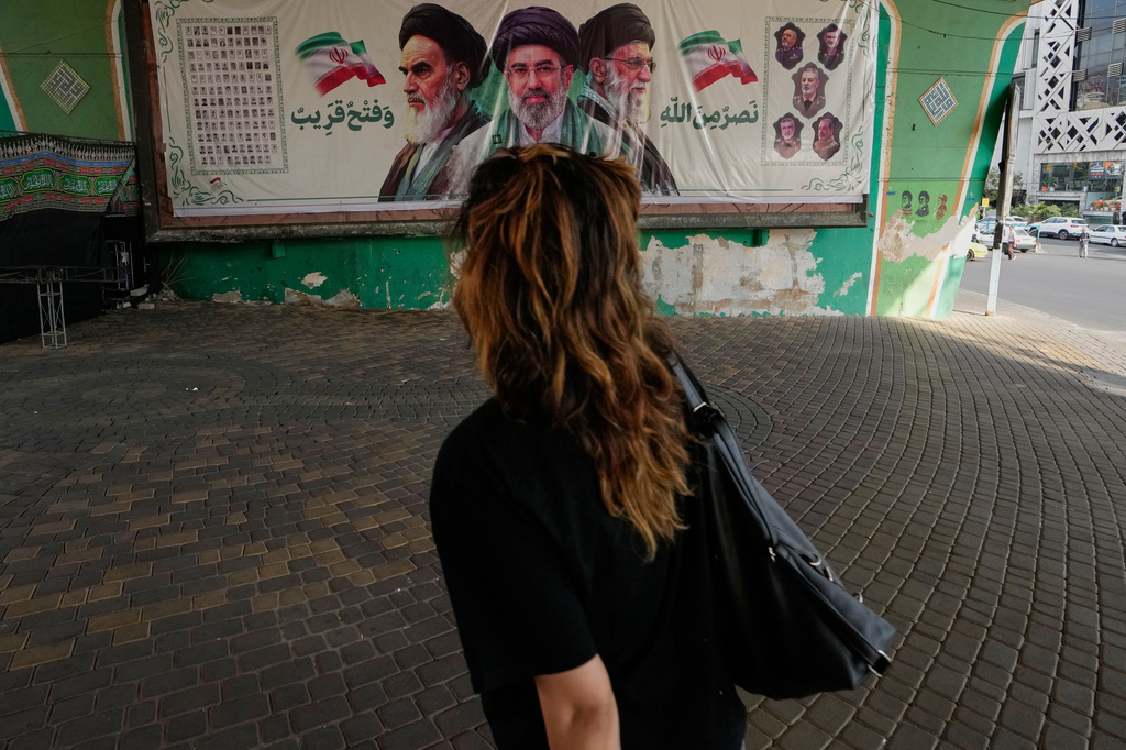 A woman walks past a banner showing portraits of the late Iranian revolutionary founder Ayatollah Khomeini, left, Supreme Leader Ayatollah Mojtaba Khamenei, center, and the late Supreme Leader Ayatollah Ali Khamenei in northern Tehran, Iran, Saturday, Sept. 12, 2026. (AP Photo/Vahid Salemi)