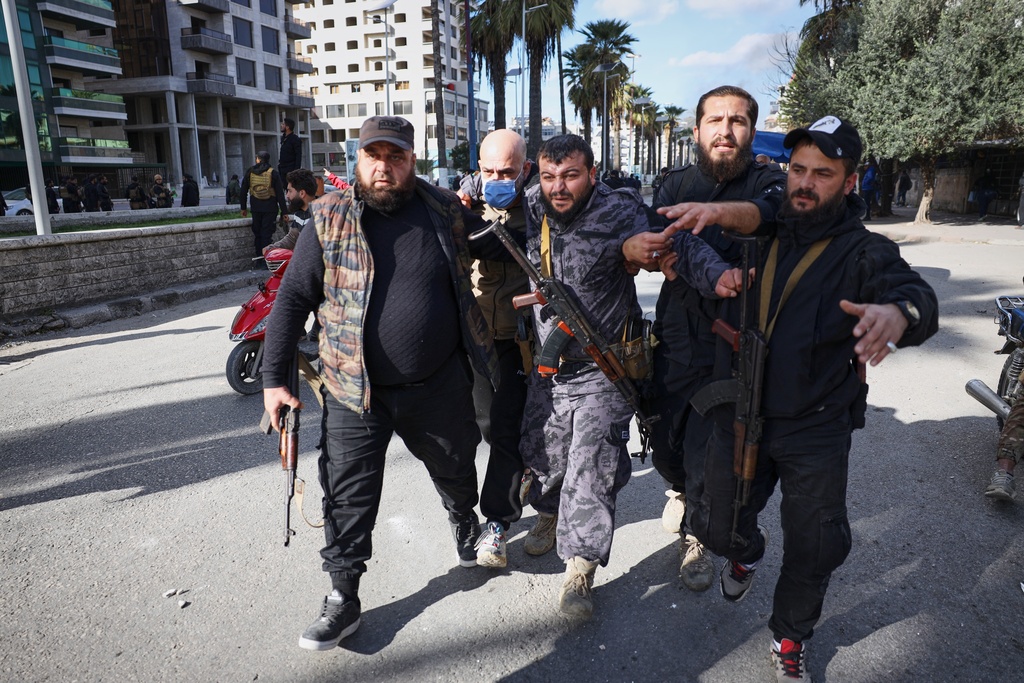 A police officer injured by a thrown stone is helped away from the area after clashes erupted between Alawite protesters from the Alawite religious minority and counterprotesters, two days after a bomb in an Alawite mosque in Homs killed eight people and wounded 18 during Friday prayers, in Latakia, Syria's coastal region, Sunday, Dec. 28, 2025. (AP Photo/Omar Albam)