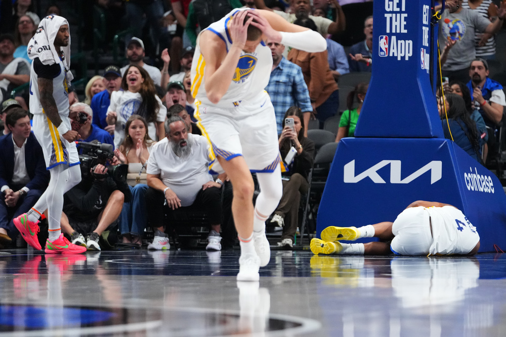 Golden State Warriors center Kristaps Porzingis, center, and guard Gary Payton II, left, react after guard Moses Moody (4) suffered an injury during overtime of an NBA basketball game against the Dallas Mavericks Monday, March 23, 2026, in Dallas. (AP Photo/Julio Cortez)