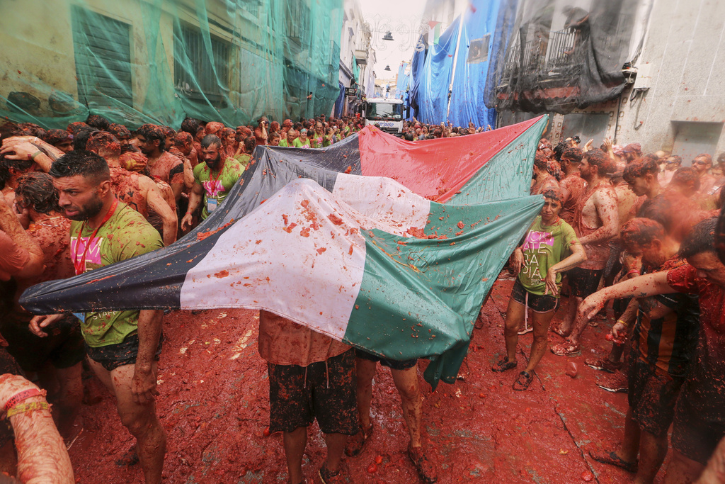 Revelers hold a Palestinian flag as they throw tomatoes at each other during the annual "Tomatina" tomato fight fiesta, in the village of Bunol near Valencia, Spain, Wednesday, Aug. 27, 2025. (AP Photo/Alberto Saiz)