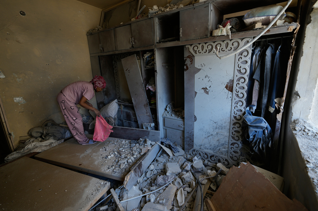 A domestic worker cleans a damaged bedroom as the homeowner returns to the house in the southern port city of Tyre, Lebanon, Thursday, April 30, 2026. (AP Photo/Hussein Malla)
