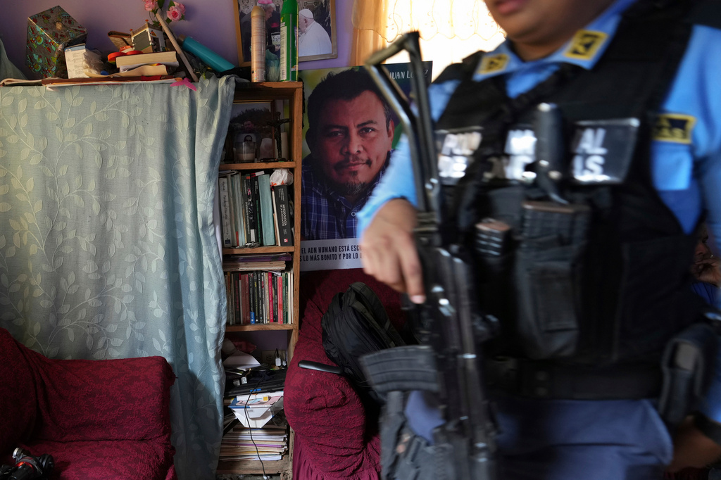 FILE - A poster of slain environmentalist Juan López hangs in his home as a state-assigned bodyguard watches over the López family, in Tocoa, Honduras, Dec. 6, 2024. (AP Photo/Moises Castillo, File)