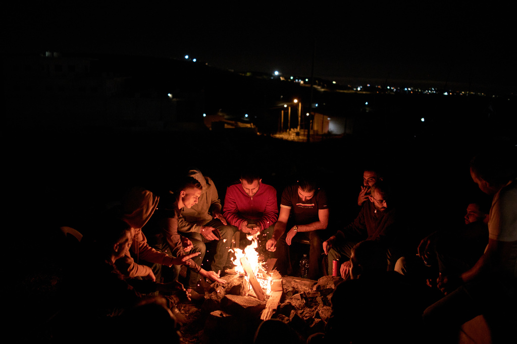 Palestinians sit next to the bonfire as they take part in a night watch to prevent Israeli settler attacks in the West Bank village of Sinjil, Thursday, July 16, 2026. (AP Photo/Leo Correa)