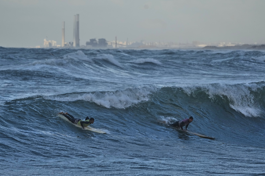 Palestinian Khalil Abu Jayyab, right, and Tahseen Abu Assi surf on the beach of Gaza City, Sunday, Dec. 28, 2025. (AP Photo/Jehad Alshrafi)