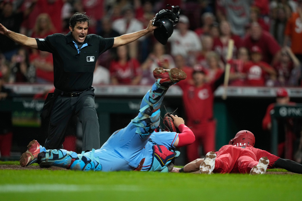 Home plate umpire John Tumpane calls Cincinnati Reds' Spencer Steer, right, safe as he dives into home plate to score the game winning run on a single hit by Blake Dunn as St. Louis Cardinals catcher Yohel Pozo, center, follows with the late tag in the eleventh inning of the second baseball game of a doubleheader in Cincinnati, Saturday, May 23, 2026. (AP Photo/Carolyn Kaster)