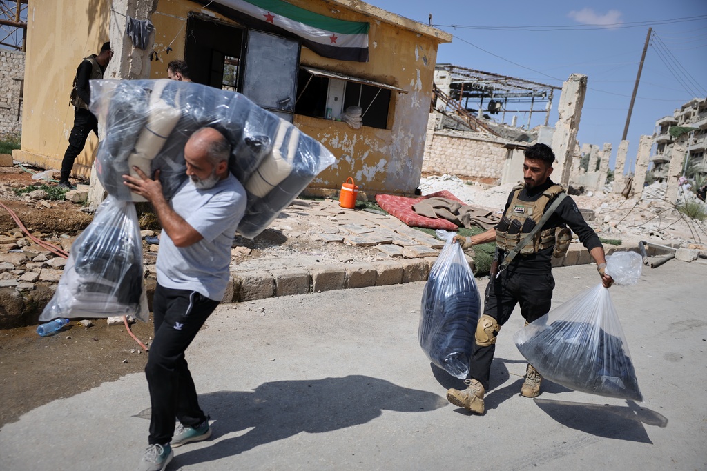 A Syrian government soldier assists a man carrying his belongings as residents leave the Sheikh Maqsoud and Achrafieh neighborhoods of Aleppo, Syria, Tuesday, Oct. 7, 2025, following overnight clashes between Syrian government troops and the Kurdish-led Syrian Democratic Forces. (AP Photo/Omar Albam)
