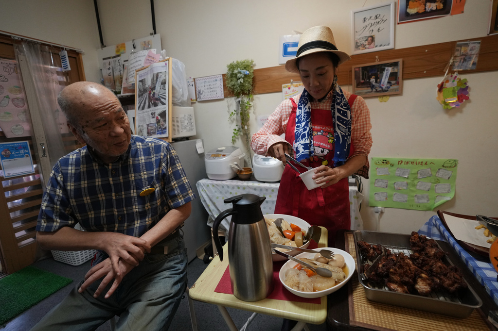 Akiko Sugaya helps her regular customer take out his buffet lunch box at her takeout lunch shop, which turns into a dine-in restaurant in the evening, in Tokyo, Saturday, July 4, 2026. (AP Photo/Hiro Komae)
