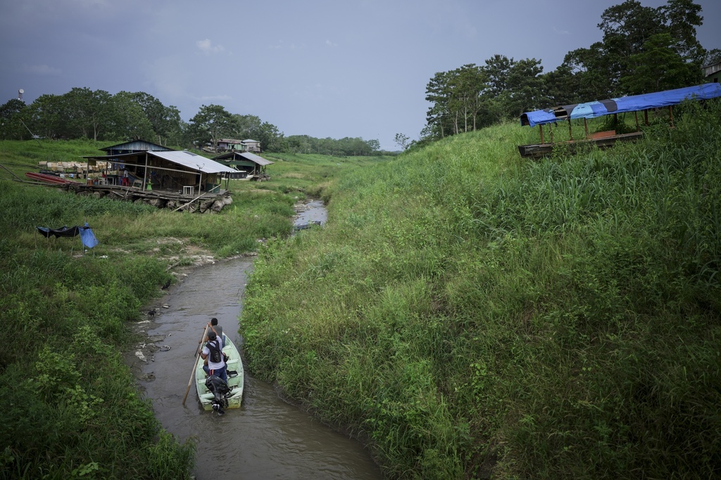 FILE - People maneuver by boat through the low water levels of a tributary that connects with the Amazon River, in Isla de la Fantasia, on the outskirts of Leticia, Colombia, Oct. 20, 2024. (AP Photo/Ivan Valencia, File)