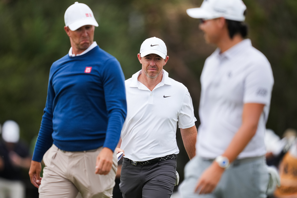 Rory McIlroy of Northern Ireland (centre) reacts after completing his round with Adam Scott of Australia (Left) and Min Woo Lee of Australia (Right) during the first round of the Australian Open golf tournament in Melbourne, Australia, Thursday, Dec. 4, 2025. (AP Photo/Asanka Brendon Ratnayake)