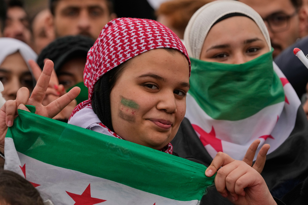 Girls flash victory signs as they gather for celebrations marking the first anniversary of the ousting of former President Bashar Assad in Damascus, Syria, Monday, Dec. 8, 2025. (AP Photo/Hussein Malla)