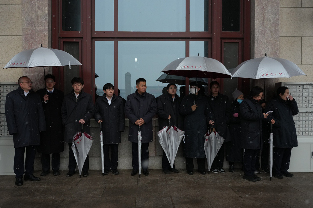 Workers stand by with umbrellas as it snows during a pre-session of the National People's Congress (NPC) at the Great Hall of the People, in Beijing, China, Wednesday, March 4, 2026. (AP Photo/Ng Han Guan)